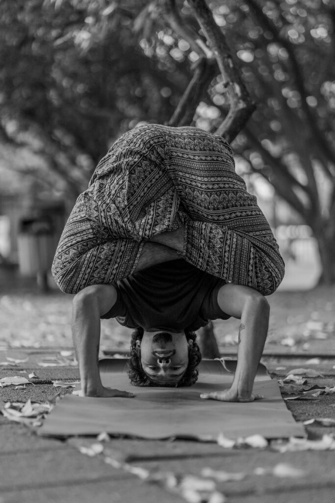A man performing a challenging headstand yoga pose on a mat outdoors.